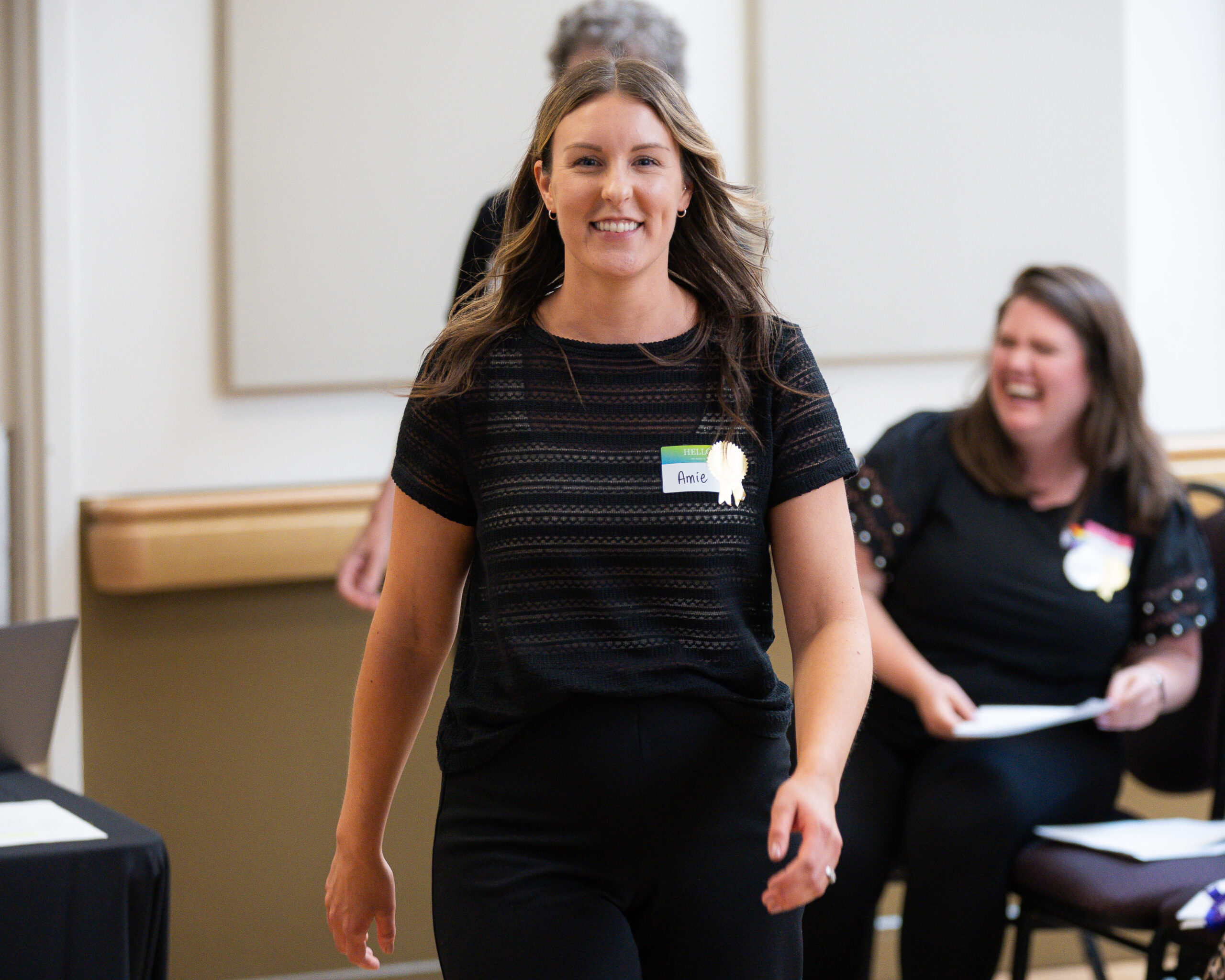 A photo of a woman in all black smiling at the camera while walking.