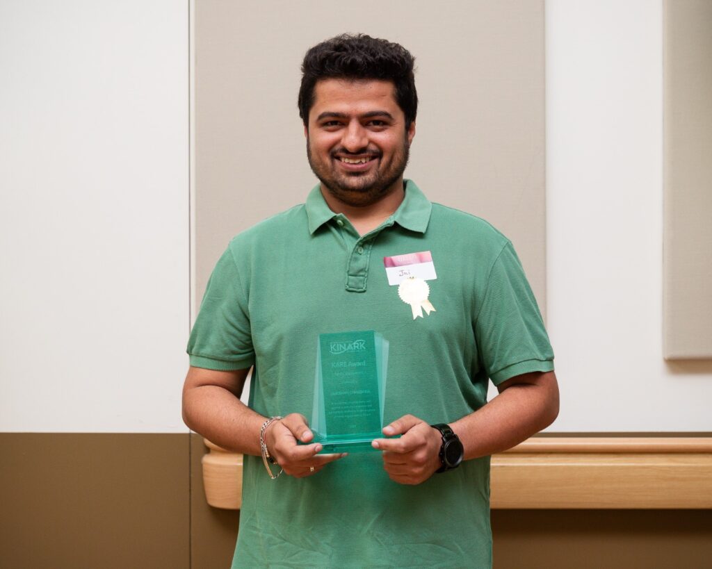 A photo of a man wearing green, smiling and holding a glass award.